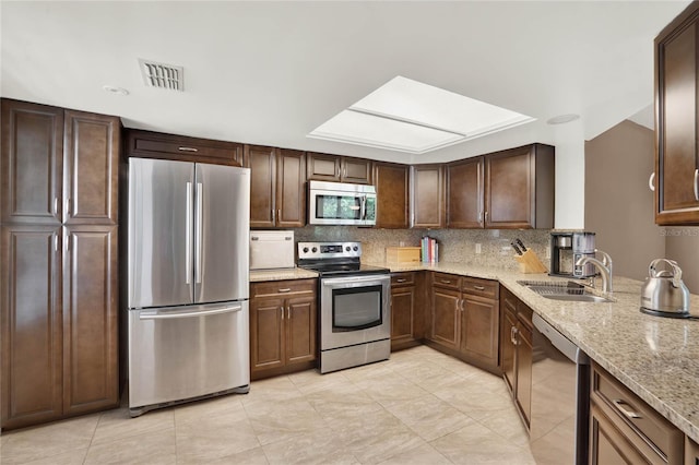 kitchen with dark brown cabinetry, sink, stainless steel appliances, light stone counters, and backsplash