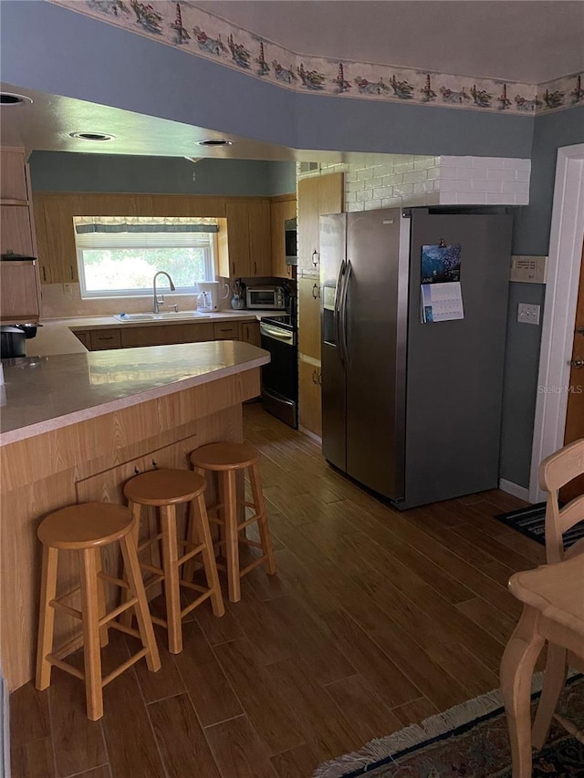 kitchen featuring electric stove, sink, stainless steel fridge with ice dispenser, kitchen peninsula, and a breakfast bar area