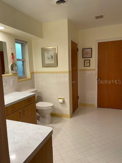 bathroom with tile patterned flooring, vanity, toilet, and tile walls