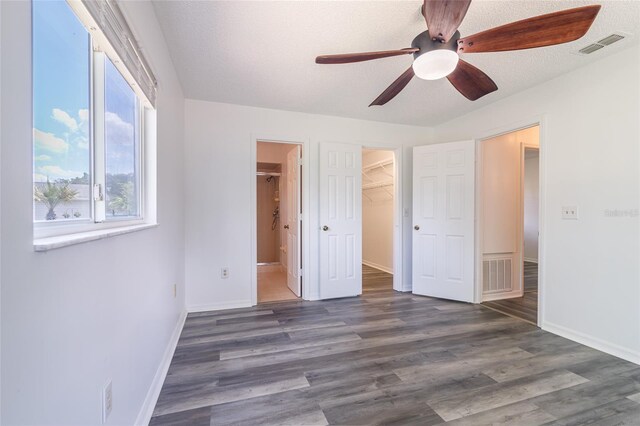 unfurnished bedroom featuring a spacious closet, a closet, ceiling fan, and dark hardwood / wood-style floors