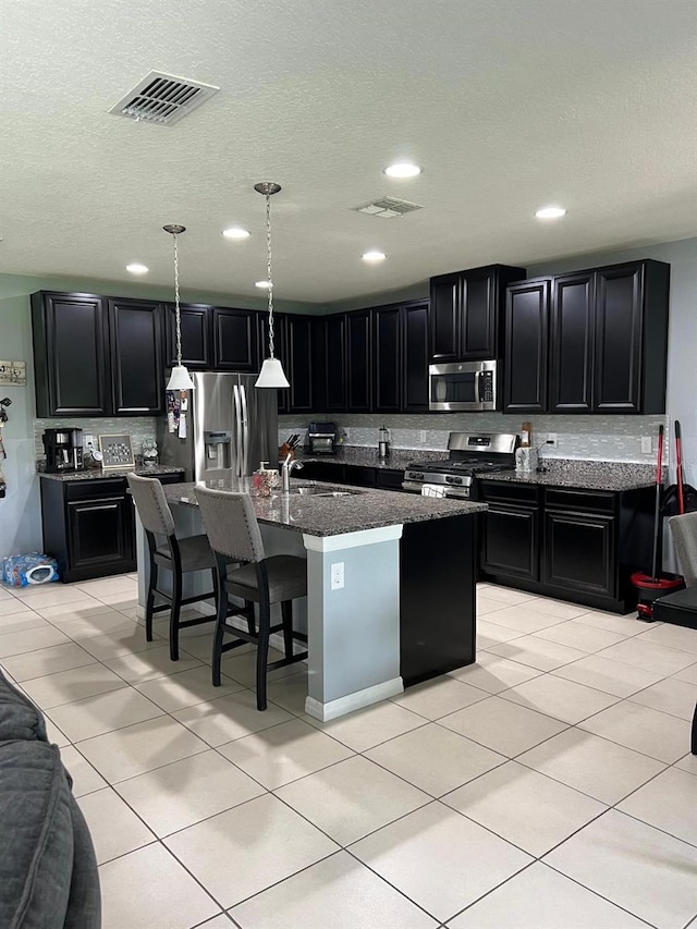 kitchen with stainless steel appliances, a center island with sink, light tile flooring, sink, and a breakfast bar