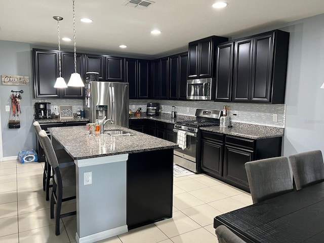 kitchen featuring stainless steel appliances, backsplash, hanging light fixtures, an island with sink, and light tile floors