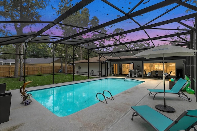 pool at dusk with a patio, a lanai, and a yard