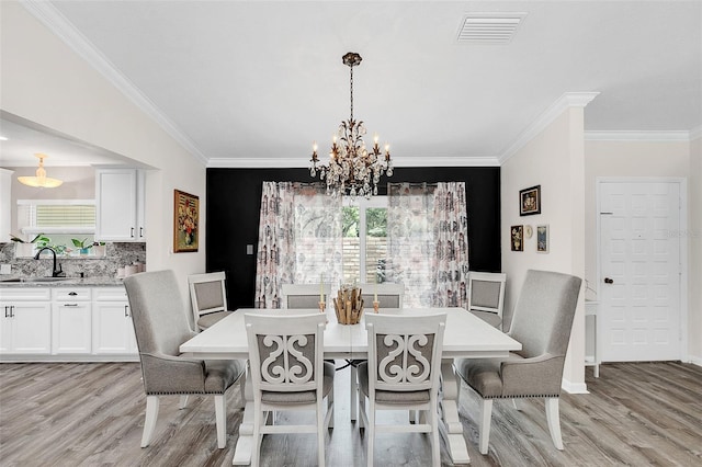 dining space with a notable chandelier, sink, light hardwood / wood-style floors, and crown molding