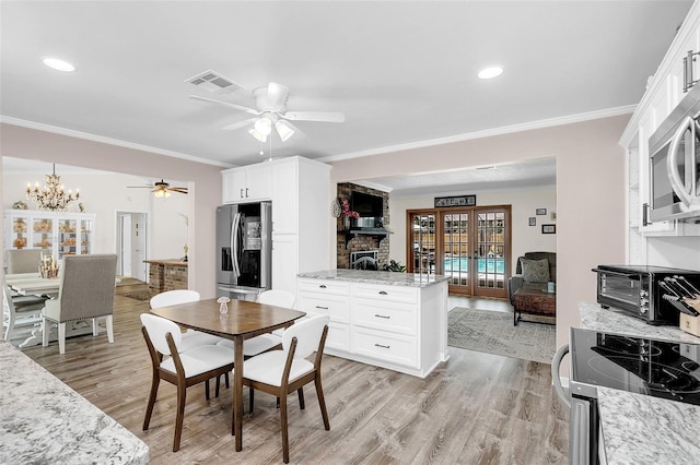 dining room featuring a stone fireplace, ornamental molding, light hardwood / wood-style flooring, and ceiling fan with notable chandelier