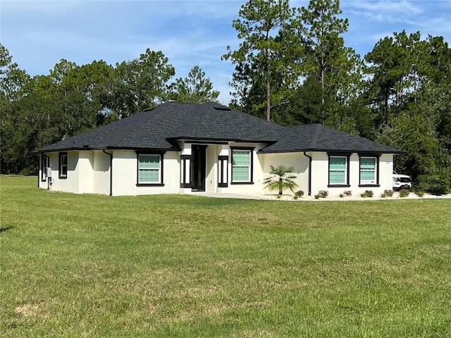 view of front facade featuring stucco siding, roof with shingles, and a front yard