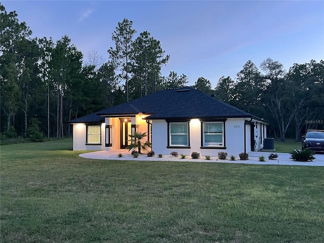 view of front of house featuring roof with shingles, central AC, and a front yard