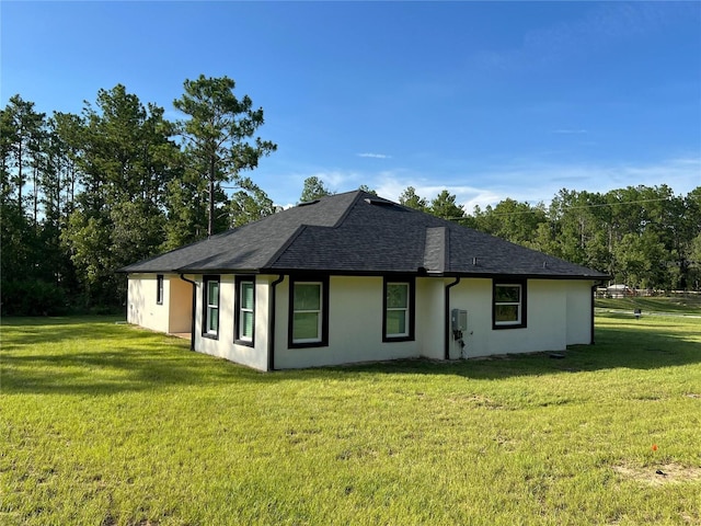 view of property exterior with a lawn, roof with shingles, and stucco siding