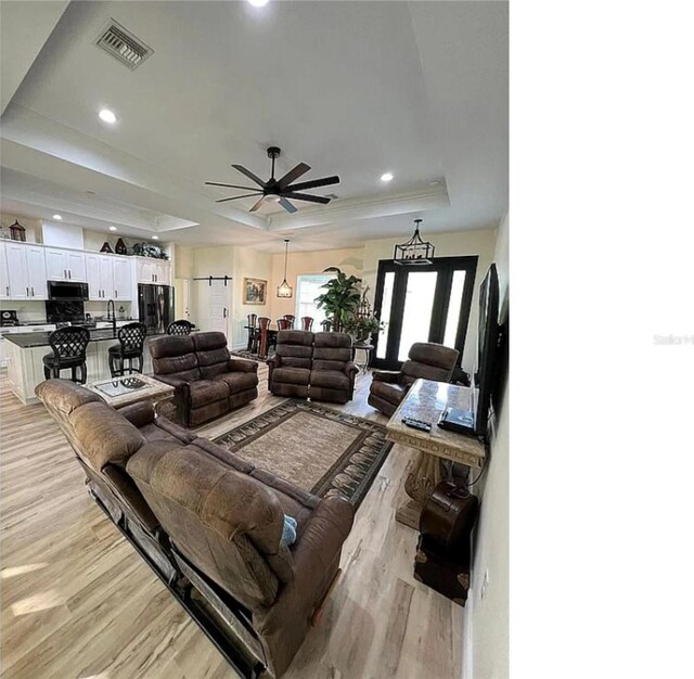 living area with light wood finished floors, visible vents, ceiling fan, a tray ceiling, and recessed lighting