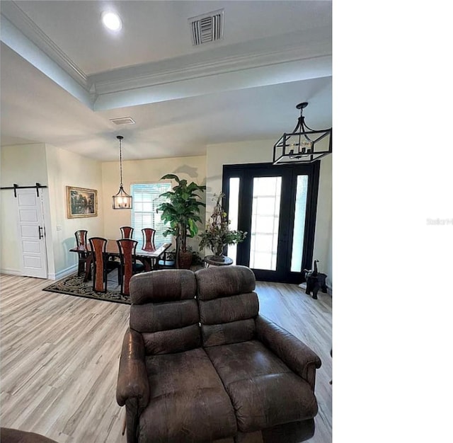 foyer entrance with a raised ceiling, light wood-type flooring, visible vents, and a chandelier