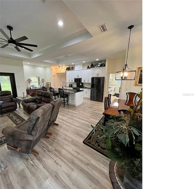 living room featuring a tray ceiling, light wood-style floors, visible vents, and ceiling fan