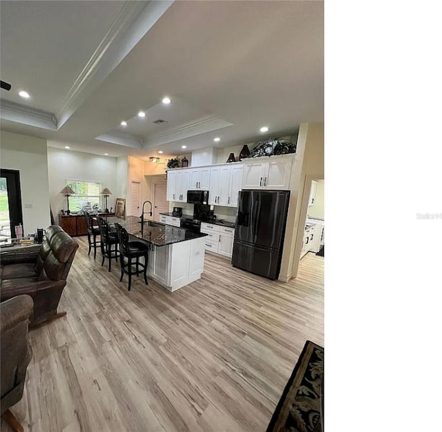 kitchen with light hardwood / wood-style floors, black appliances, an island with sink, and a tray ceiling