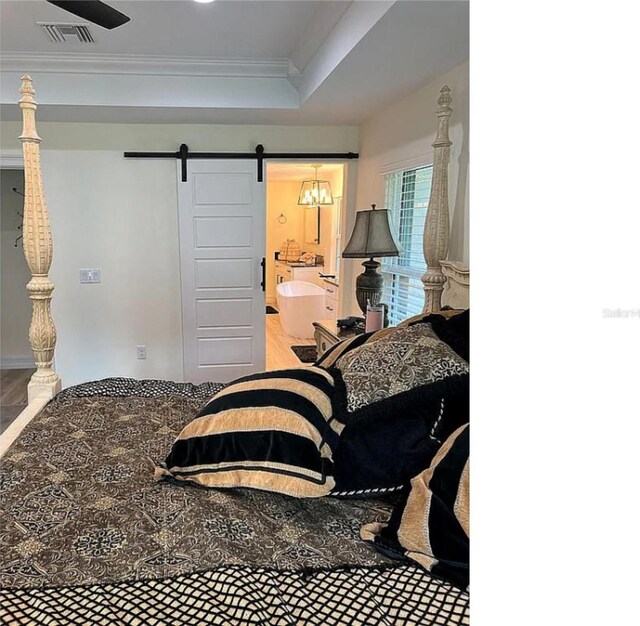 bedroom with ornamental molding, hardwood / wood-style flooring, a raised ceiling, and a barn door