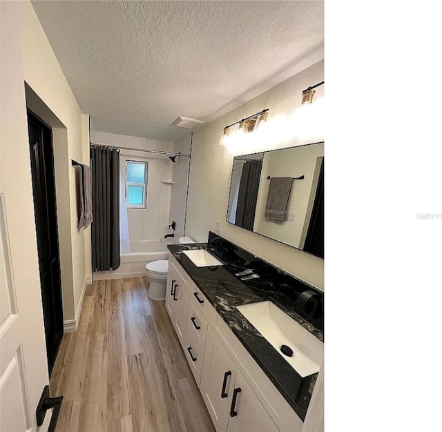 full bathroom with a textured ceiling, shower / tub combo with curtain, toilet, hardwood / wood-style flooring, and dual bowl vanity