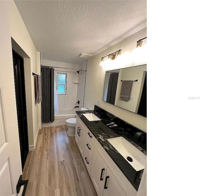 bathroom featuring toilet, shower / bath combo with shower curtain, wood finished floors, a textured ceiling, and a sink