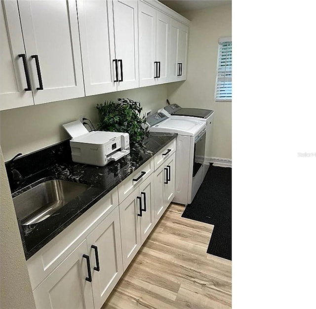 laundry room with light wood-type flooring, a sink, washing machine and dryer, cabinet space, and baseboards