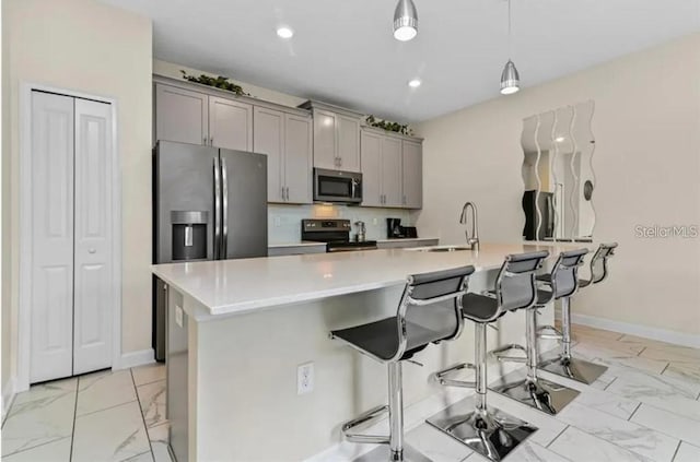 kitchen with gray cabinetry, sink, a breakfast bar area, a center island with sink, and appliances with stainless steel finishes