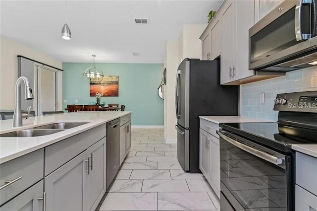 kitchen with gray cabinetry, an inviting chandelier, sink, decorative light fixtures, and stainless steel appliances