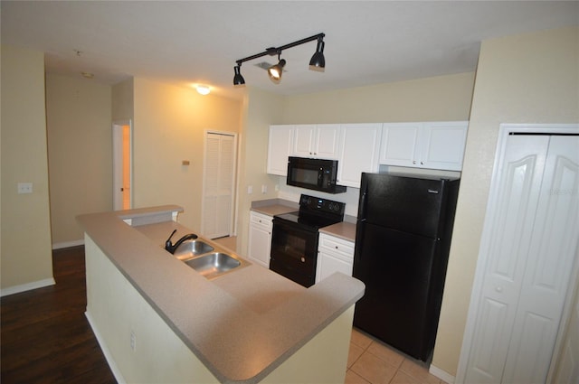 kitchen featuring a kitchen island with sink, a sink, baseboards, white cabinets, and black appliances