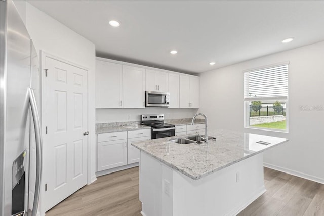 kitchen with a kitchen island with sink, sink, light wood-type flooring, white cabinetry, and appliances with stainless steel finishes