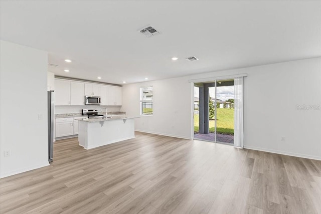 kitchen with light hardwood / wood-style floors, white cabinets, stainless steel appliances, and a center island with sink