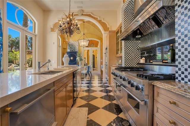 kitchen with decorative backsplash, hanging light fixtures, appliances with stainless steel finishes, light stone countertops, and a chandelier