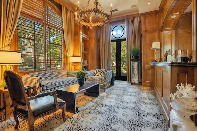 sitting room featuring a towering ceiling, french doors, an inviting chandelier, and wood walls