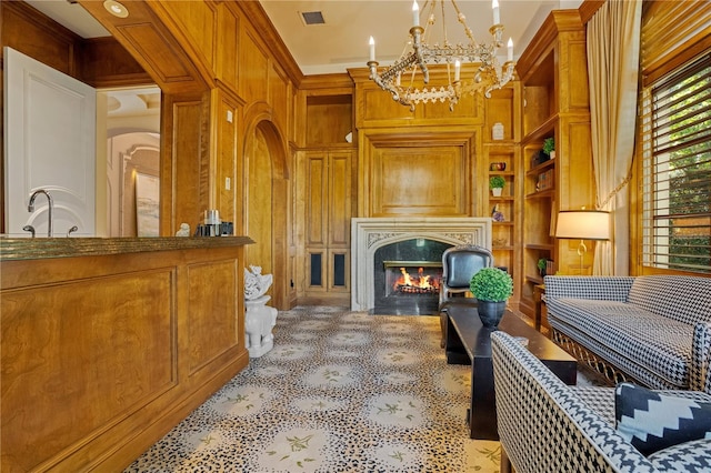 living area with wooden walls, sink, crown molding, an inviting chandelier, and a fireplace