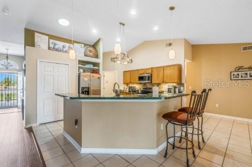 kitchen featuring stainless steel appliances, dark countertops, decorative light fixtures, and brown cabinets