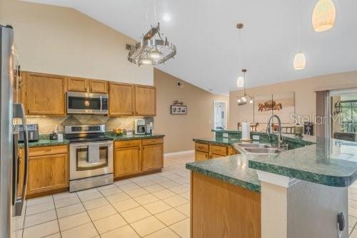 kitchen featuring appliances with stainless steel finishes, dark countertops, hanging light fixtures, and an island with sink