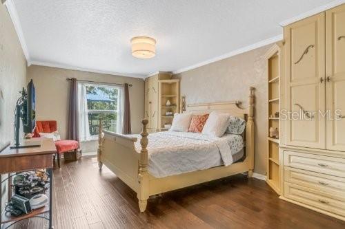 bedroom featuring crown molding, baseboards, dark wood finished floors, and a textured ceiling