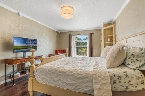 bedroom with a textured ceiling, a textured wall, baseboards, ornamental molding, and dark wood finished floors