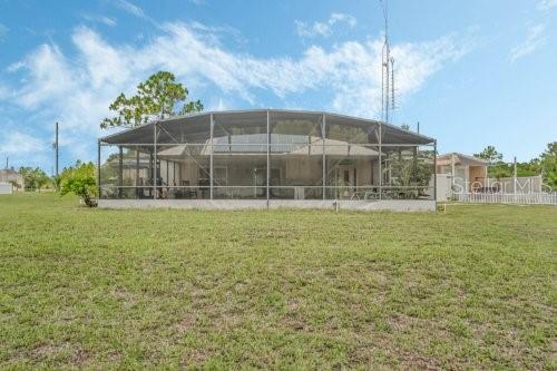 back of property featuring glass enclosure and a lawn