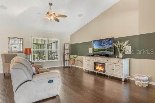 living area featuring high vaulted ceiling, dark wood-style flooring, a ceiling fan, baseboards, and a glass covered fireplace