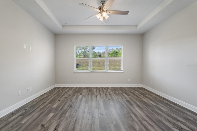 empty room with a textured ceiling, ceiling fan, dark wood-type flooring, and a tray ceiling