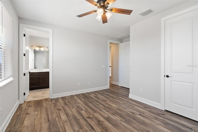 unfurnished bedroom with ensuite bathroom, ceiling fan, dark hardwood / wood-style floors, and multiple windows