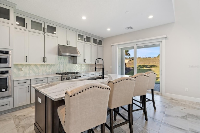 kitchen featuring light stone countertops, tasteful backsplash, a breakfast bar, a kitchen island with sink, and sink