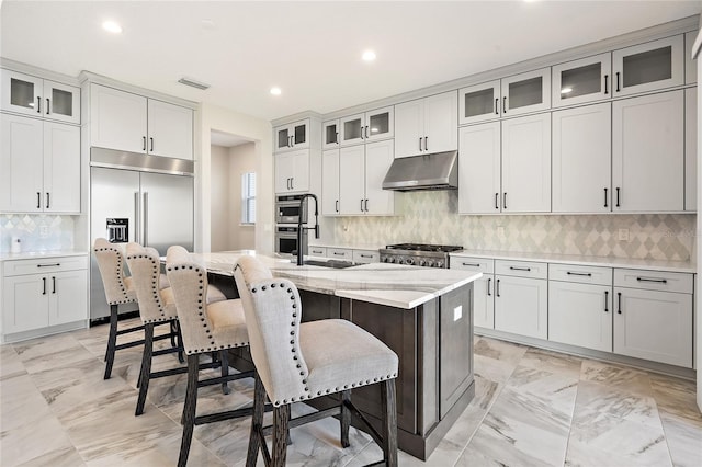 kitchen with white cabinetry, a center island with sink, stainless steel built in refrigerator, and range