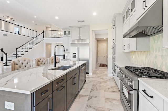 kitchen with light stone countertops, high end appliances, a kitchen island with sink, sink, and white cabinetry