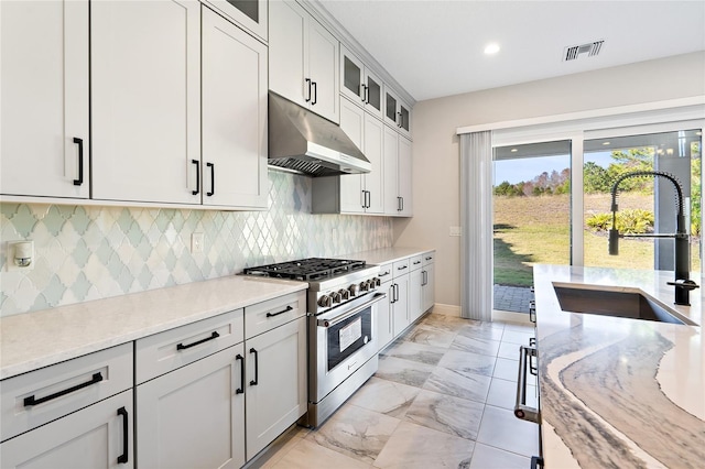 kitchen featuring sink, stainless steel range, tasteful backsplash, light stone counters, and white cabinetry