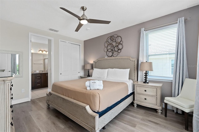 bedroom featuring ceiling fan, light hardwood / wood-style floors, a closet, and ensuite bath