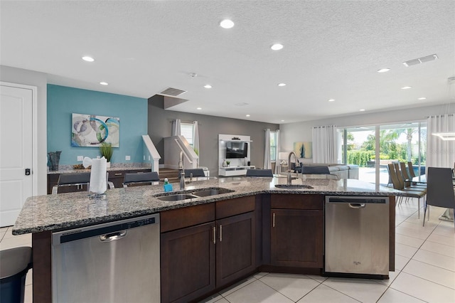 kitchen with a textured ceiling, dishwasher, sink, and an island with sink