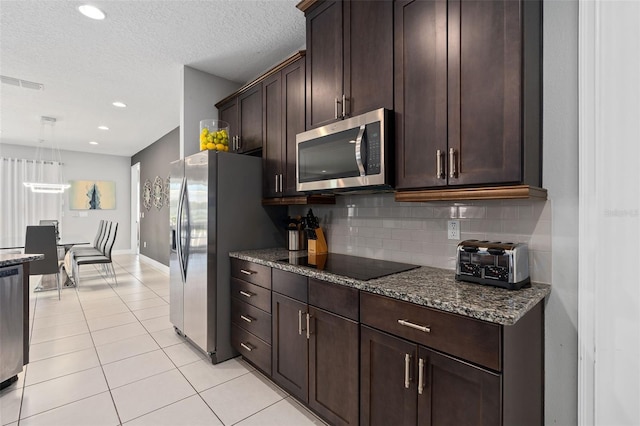 kitchen featuring backsplash, stone counters, light tile patterned floors, appliances with stainless steel finishes, and dark brown cabinetry