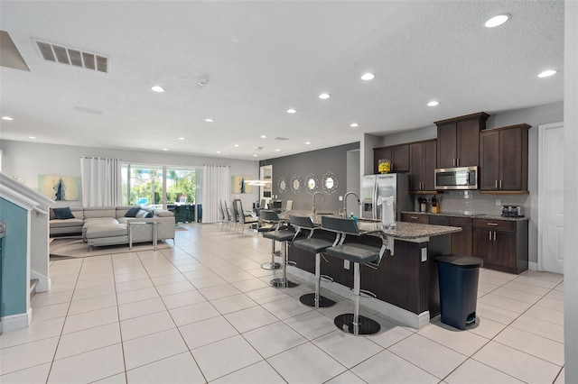 kitchen featuring a kitchen bar, light stone counters, stainless steel appliances, a center island with sink, and light tile patterned flooring