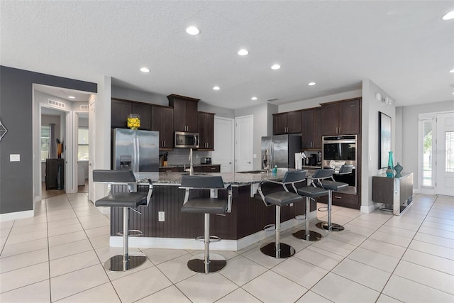 kitchen featuring a breakfast bar, dark brown cabinets, stainless steel appliances, and a large island with sink