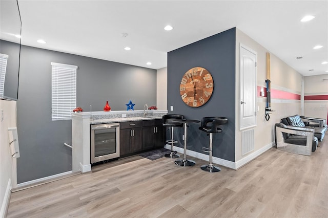 bar featuring dark brown cabinetry, sink, wine cooler, and light hardwood / wood-style flooring