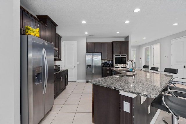 kitchen with a center island with sink, a kitchen breakfast bar, sink, dark stone countertops, and appliances with stainless steel finishes