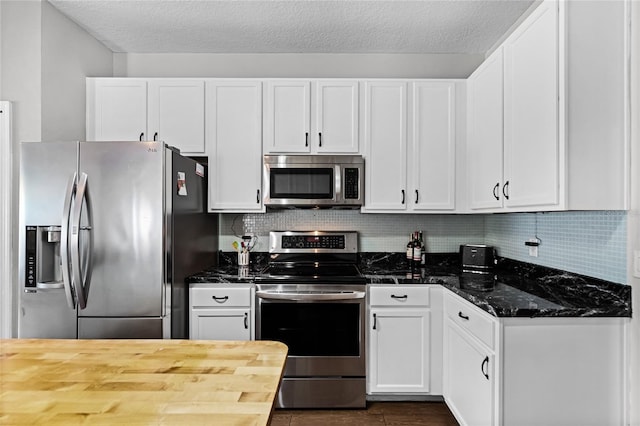 kitchen featuring appliances with stainless steel finishes, dark stone counters, white cabinets, and decorative backsplash