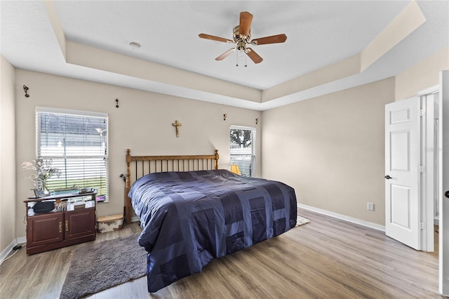 bedroom with light wood-style floors, baseboards, a tray ceiling, and a ceiling fan