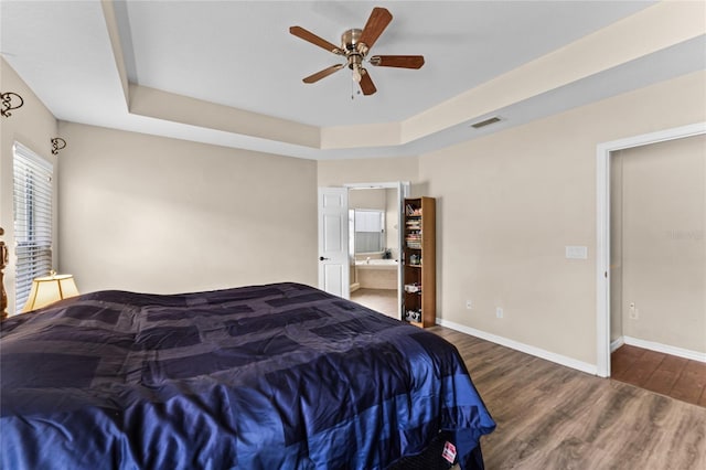 bedroom featuring a tray ceiling, dark wood finished floors, visible vents, connected bathroom, and baseboards